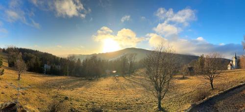 a sun setting over a field with a mountain at Penzion Soukupovi in Strážné