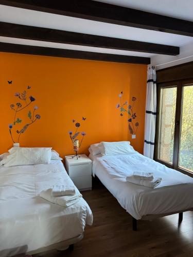 two beds in a bedroom with an orange wall at El Roble, casitas rurales in Valverde de la Vera