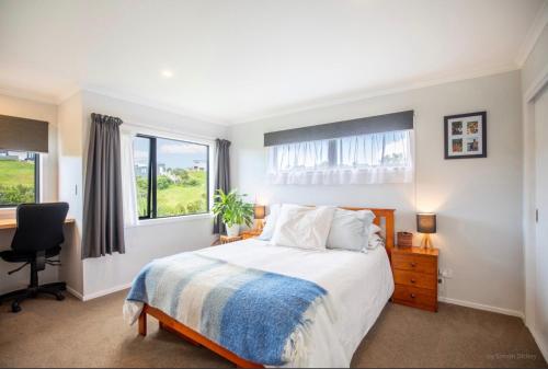 a bedroom with a bed and a desk and windows at Raglan Sun Seekers Retreat in Raglan