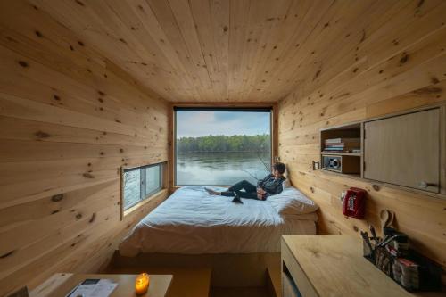 una donna seduta su un letto in una stanza con finestra di Postcard Cabins Talladega Valley, Outdoor Collection by Marriott Bonvoy a Childersburg