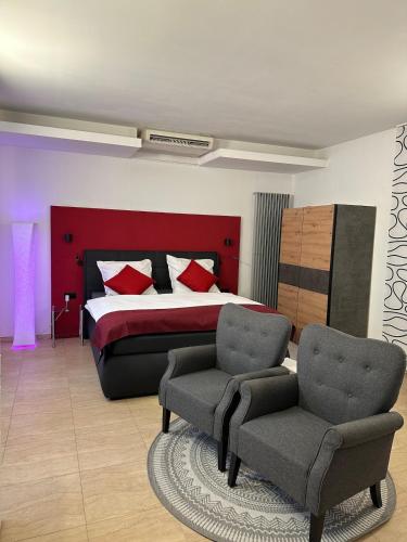a bedroom with a bed with a red headboard and two chairs at Private Spa Suite bei Heilbronn - Romantik, Wellness & absolute Privatsphäre in Massenbachhausen