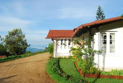 a white house with a red roof next to a dirt road at Windermere Estate in Munnar
