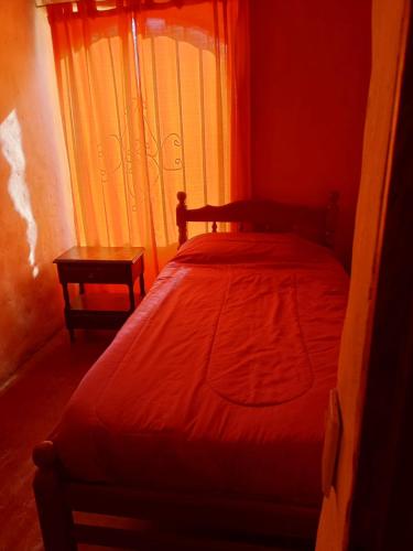 a bedroom with a bed with a red comforter and a window at Nativas Cabaña Amarilla in Senador Pérez