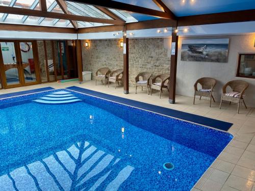 a swimming pool in a building with chairs around it at Coombehayes Barn in Uplyme