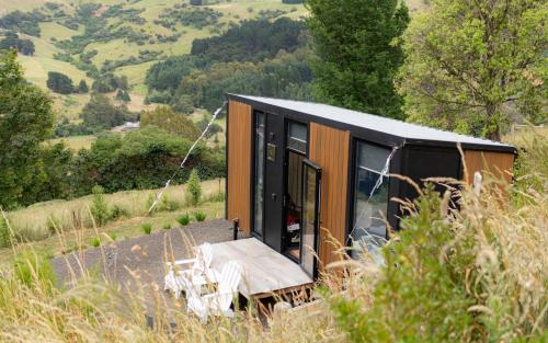 een klein huisje met een veranda en stoelen op een heuvel bij Kūkupa Puni at Akaroa Lavender by Tiny Away in Akaroa