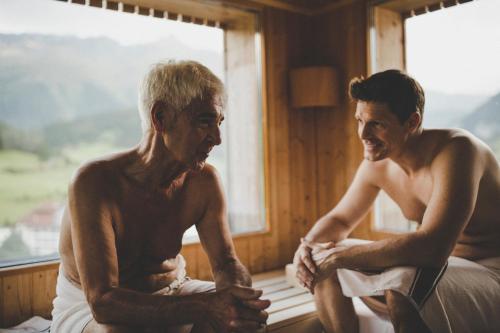 a man and a man sitting on a bed next to a window at Arabella Retreat & Spa in Nauders
