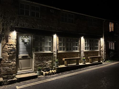 een stenen gebouw met 's nachts twee bankjes buiten bij Priory Weavers Cottage in Burford