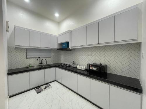 a kitchen with white cabinets and a black counter top at Farisya Homestay in Kota Bharu
