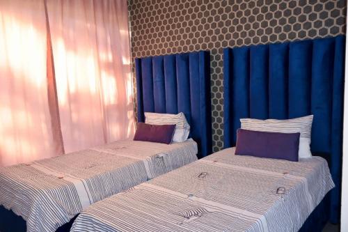 zwei Betten in einem Zimmer mit blauen Vorhängen in der Unterkunft San Remo on Windermere Rd. Humewood Beachfront in Gqeberha