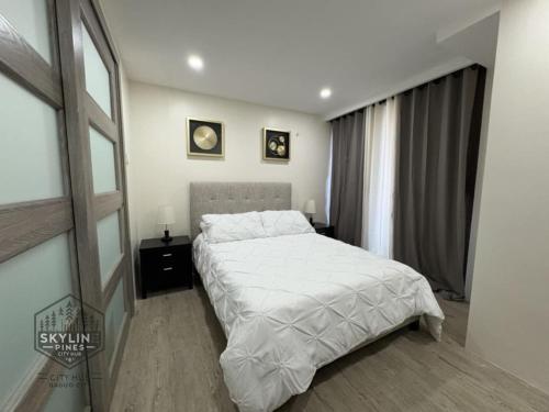 ein Schlafzimmer mit einem weißen Bett und einem Fenster in der Unterkunft Skyline Pines City Hub - Baguio in Baguio City
