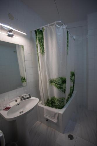 a bathroom with a sink and a shower curtain with a plant at Hostal Residencia Avenida in Cuenca