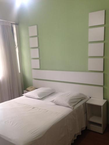 a bedroom with a white bed with a green wall at Hotel Turista in Belo Horizonte