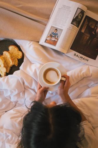 Een vrouw ligt in bed met een kop koffie en een tijdschrift. bij Auberge du Rédier - Logis Hôtels in Colomars