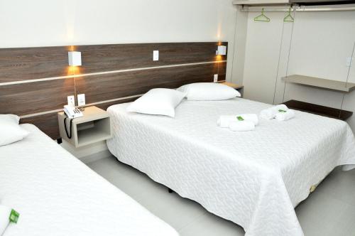 duas camas num quarto de hotel com lençóis brancos e toalhas em Hotel Villa Cerrado em Nova Mutum