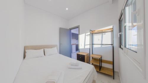 a white bedroom with a bed and a window at Delfini Girni Apartments in Paralia Katerinis