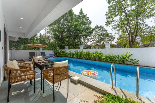 a patio with a table and chairs next to a swimming pool at ELIVAAS Signature Casa Del Mundo With Pvt Pool, Bar, Lift & Scenic Hill Vistas in Vagator