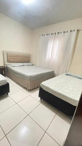 two beds sitting in a room with white tiles at Descanso e aconchego in Aparecida