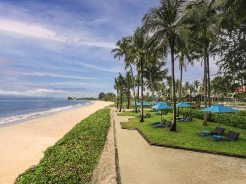 una playa con palmeras y sombrillas azules en Grand Mercure Khao Lak Bangsak, en Khao Lak
