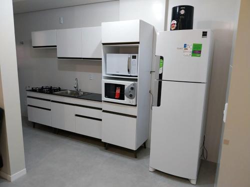 eine weiße Küche mit einem Kühlschrank und einer Mikrowelle in der Unterkunft Modern apartment steps from the beach with amenities in Arroio do Silva