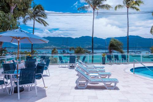 a patio with chairs and a pool with mountains in the background at Hotel Ilhabela in Ilhabela