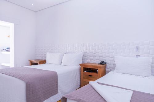 two beds in a room with white walls at Hotel Ilhabela in Ilhabela