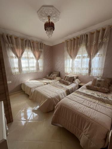three beds in a room with windows and a chandelier at Ideal Tetuan in Tétouan