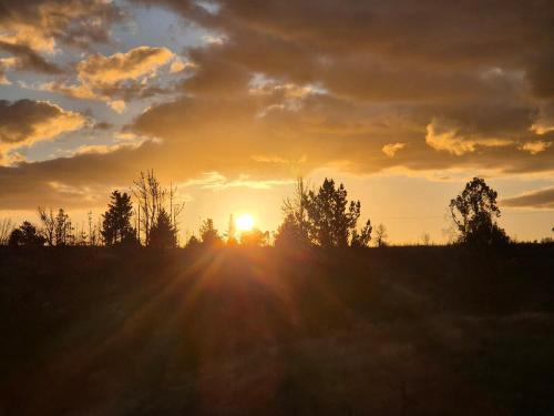 a sunset over a field with trees in the background at Hermosa Cabaña en medio de la naturaleza in Los Angeles