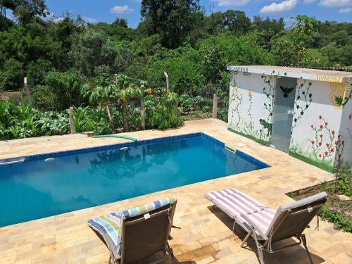 a swimming pool in a garden with two chairs next to it at Casa sitio , Elias Fausto Campinas in Elias Fausto