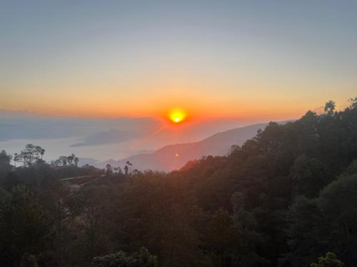 a sunset in the mountains with the sun setting over the trees at Hotel Pigeon Prince in Nagarkot