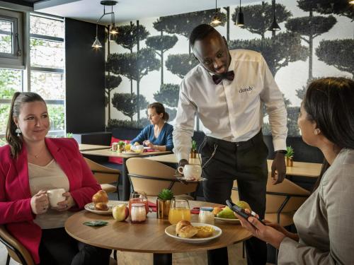 a man in a bow tie standing at a table in a restaurant at Novotel Suites Paris CDG Airport Villepinte in Roissy-en-France