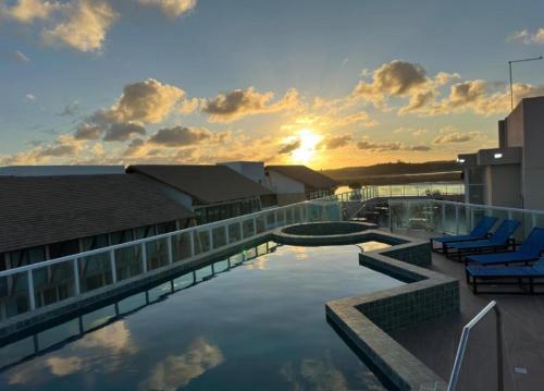 een gebouw met een zwembad met ligstoelen en de zonsondergang bij Eco mirage Residence in Porto De Galinhas