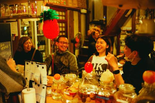 a group of people sitting at a table with food at Hostel&Bar CAMOSIBA in Yokote
