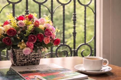 a vase of flowers sitting on a table with a cup of coffee at Golden Queen Aparthotel in Ho Chi Minh City
