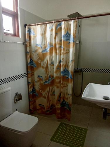 a bathroom with a shower curtain with a toilet and a sink at New Hotel Bundala park in Tissamaharama