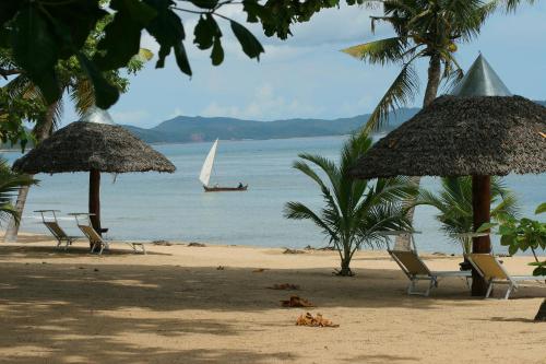 a beach with chairs and umbrellas and a boat in the water at Eden Lodge in Madirokely