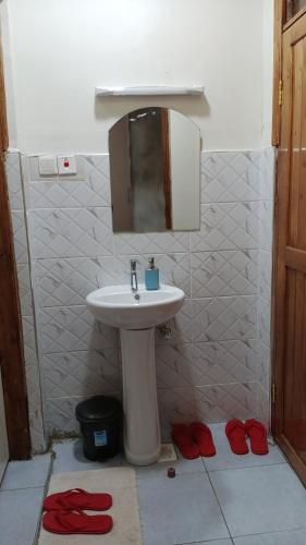 ein Bad mit einem Waschbecken, einem Spiegel und roten Hausschuhen in der Unterkunft Serene Stays in Naivasha