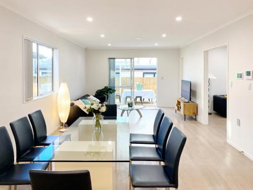 a dining room and living room with a glass table and chairs at Modern New Home on Dungloe Ave, Central AC, 2 Kitchens, 3 livings in Auckland