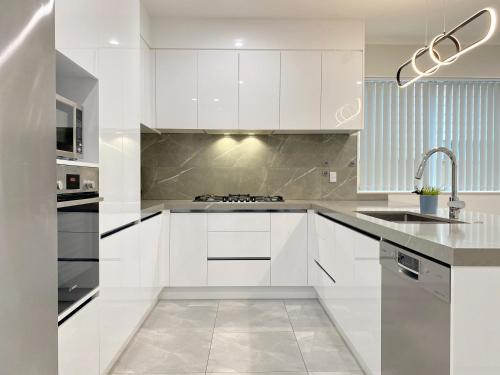 a white kitchen with white cabinets and a sink at Modern New Home on Dungloe Ave, Central AC, 2 Kitchens, 3 livings in Auckland