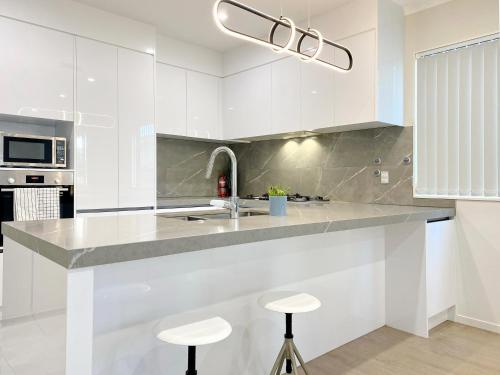 a kitchen with white cabinets and a sink and stools at Modern New Home on Dungloe Ave, Central AC, 2 Kitchens, 3 livings in Auckland