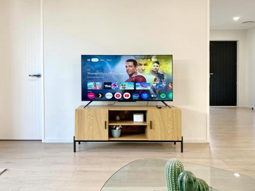 a flat screen tv on a wooden stand in a living room at Modern New Home on Dungloe Ave, Central AC, 2 Kitchens, 3 livings in Auckland