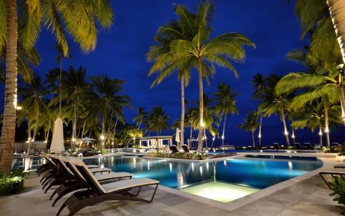 a pool with chairs and palm trees at night at Henann Resort Alona Beach in Panglao
