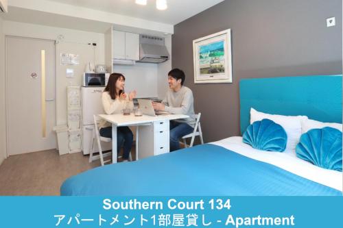 a man and woman sitting at a table in a bedroom at Enoshima Guest House 134 in Fujisawa