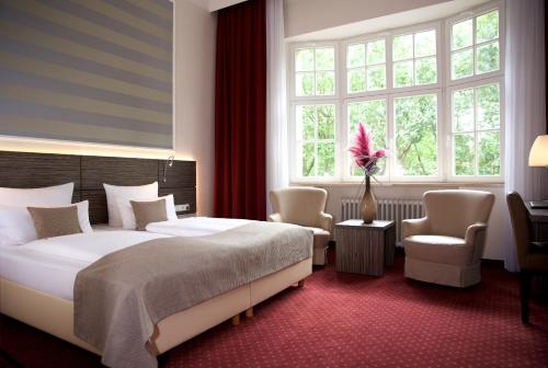 a bedroom with a bed and two chairs and a window at Hotel Prinzregent in Nürnberg