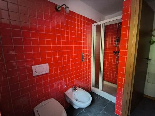 a red tiled bathroom with a toilet and a shower at WHITE ALPS Apartment in Schilpario
