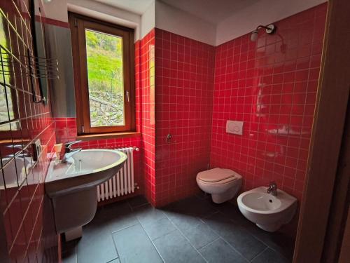a red tiled bathroom with a toilet and a sink at WHITE ALPS Apartment in Schilpario