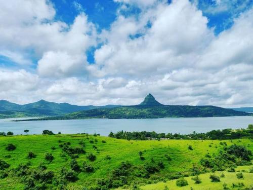 ein grünes Feld mit einem See und einem Berg in der Unterkunft Vrindavan Hotel and Restaurant in Malavli