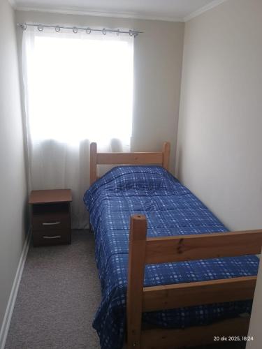 a bedroom with a bed with a blue comforter and a window at M&L departamento in Limache