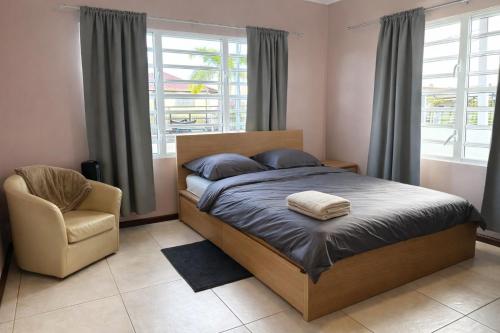 ein Schlafzimmer mit einem Bett und einem Stuhl und Fenstern in der Unterkunft Maison Meredith in Paramaribo