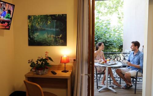 Ein Mann und eine Frau, die an einem Tisch auf einem Balkon sitzen in der Unterkunft Hôtel Belleville in Lamalou-les-Bains