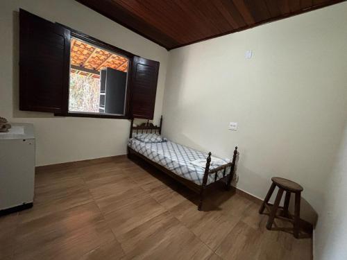 a room with a bed and a window and a stool at Cantinho da Serra do Cipó in Santana do Riacho